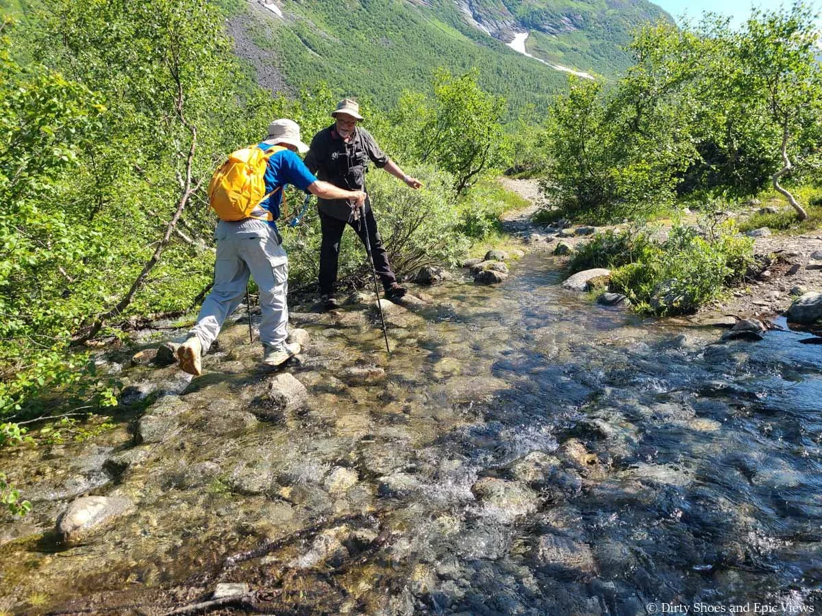 A hiker uses trekking poles to cross a stream on the Austerdalsbreen hike in Norway