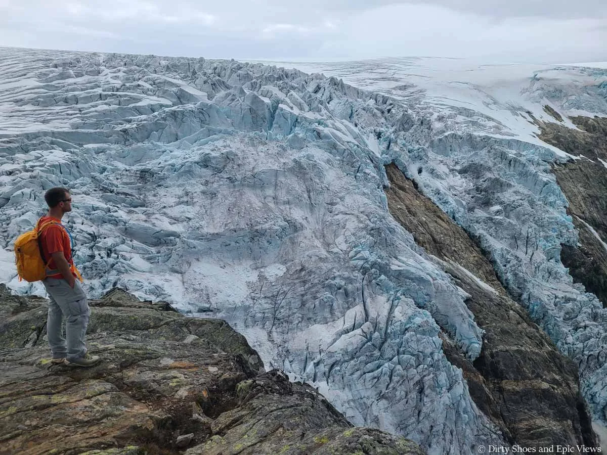 A hiker stands at a viewpoint overlooking a massive icecap and glacier from the Reinanuten viewpoint in Norway