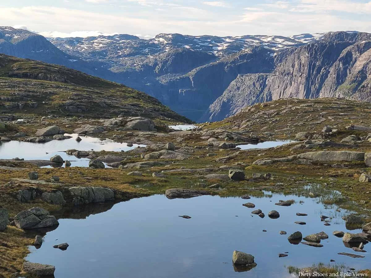 Still tarns dot a grassy meadow in front of a mountain backdrop along the Trolltunga trail in Norway