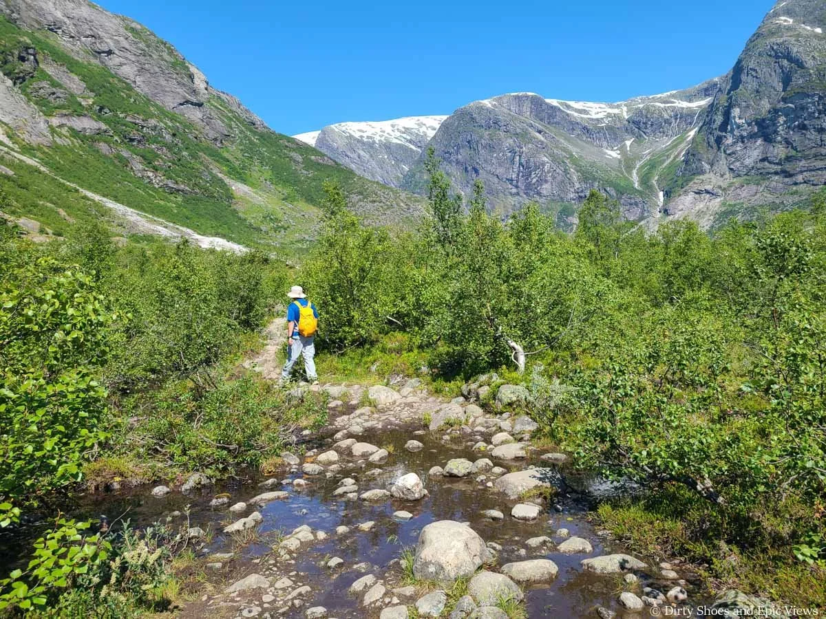 A hiker walks along a rocky path across a stream on the Austerdalsbreen hike
