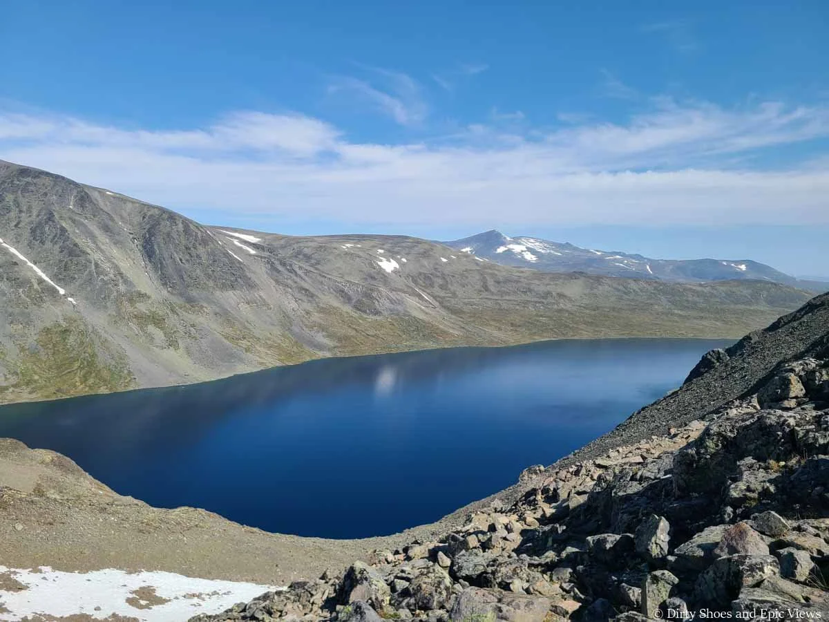 A deep blue lake is surrounded by hills as seen from the Besseggen Ridge trail in Norway