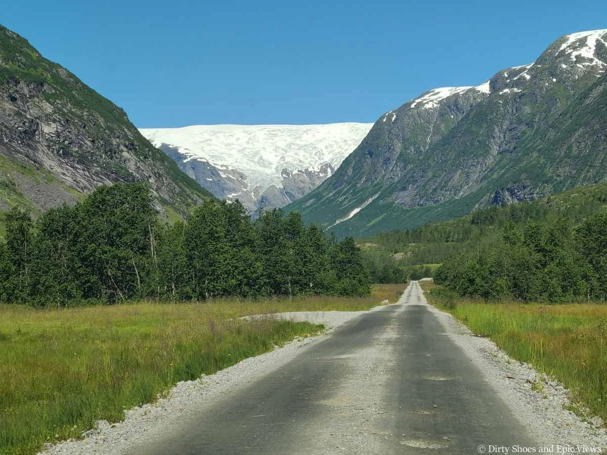 A flat wide gravel road heads towards views of mountains and glaciers on the Austerdalsbreen toll road