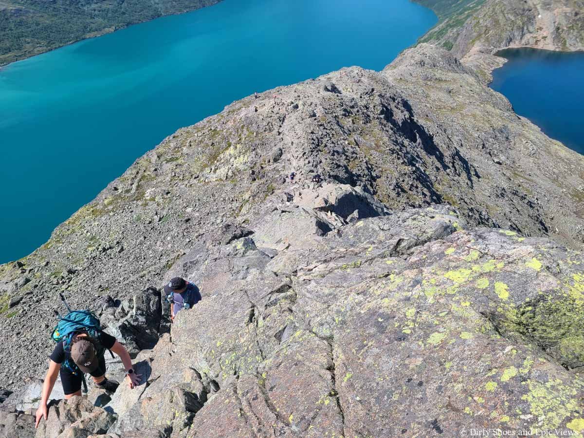 Looking down on a pair of hikers ascending a rocky ridge above two lakes on the Besseggen Ridge trail in Norway