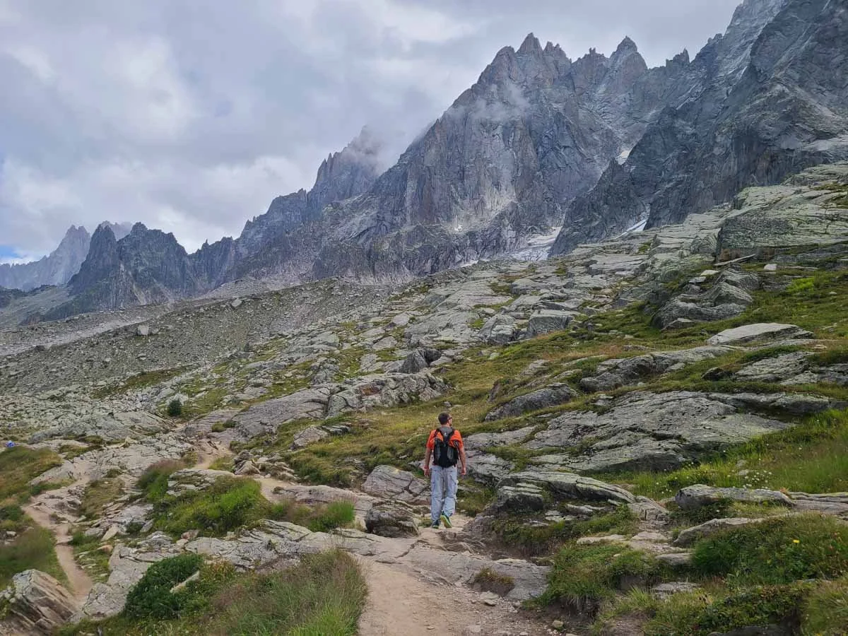 A hiker on a rocky trail to Lac Bleu in Chamonix with jagged mountain peaks in the distance