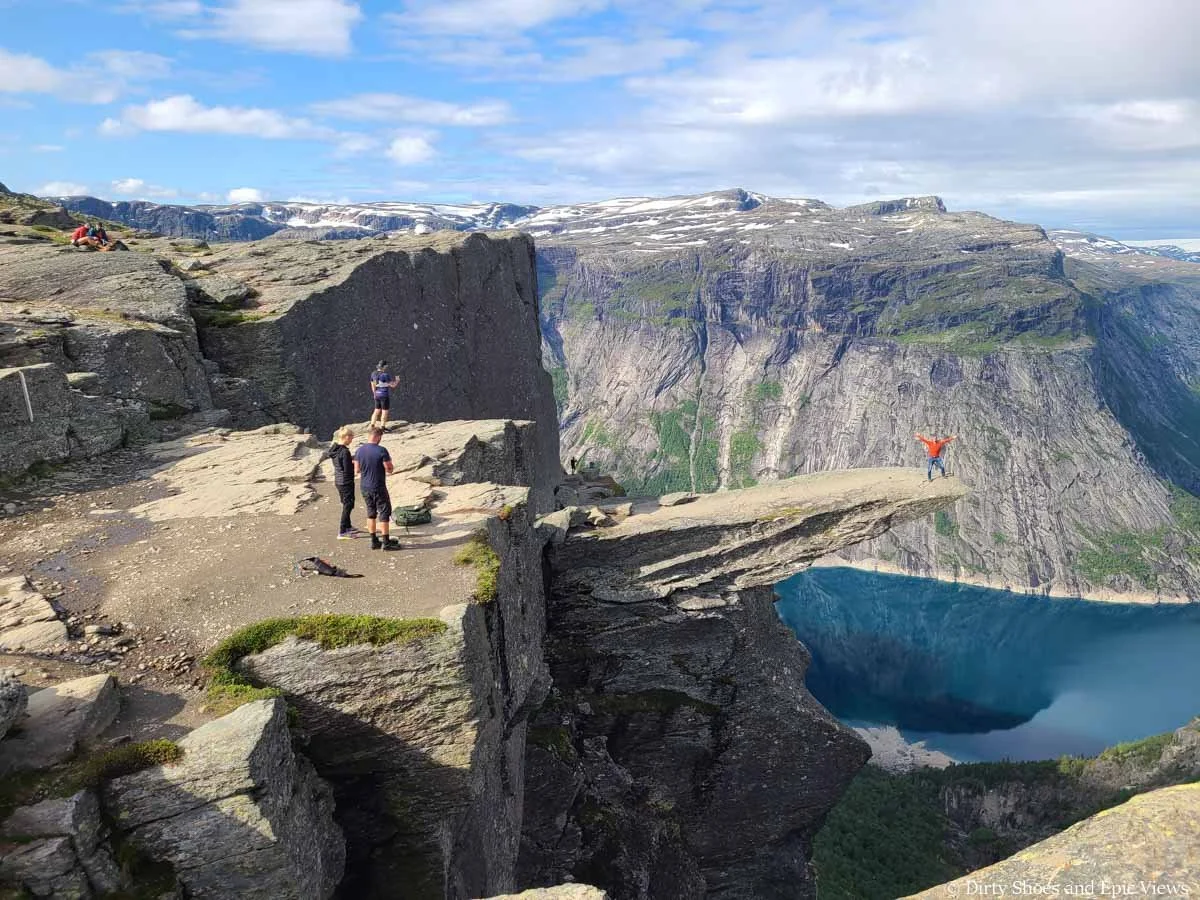 A couple of people stand on the edge of a cliff taking pictures of someone posing on Trolltunga