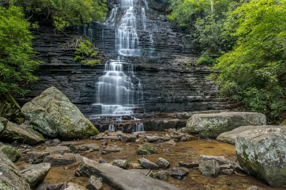 Benton waterfall cascading down a rocky cliff surrounded by green trees and rocks in a forest.