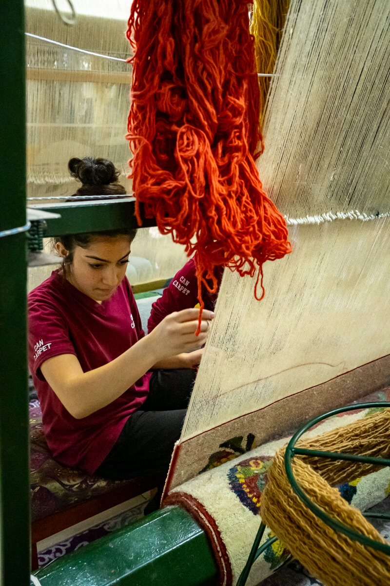 A woman weaves carpets by hand on a loom. Each carpet takes anywhere from 3-12 months to complete.