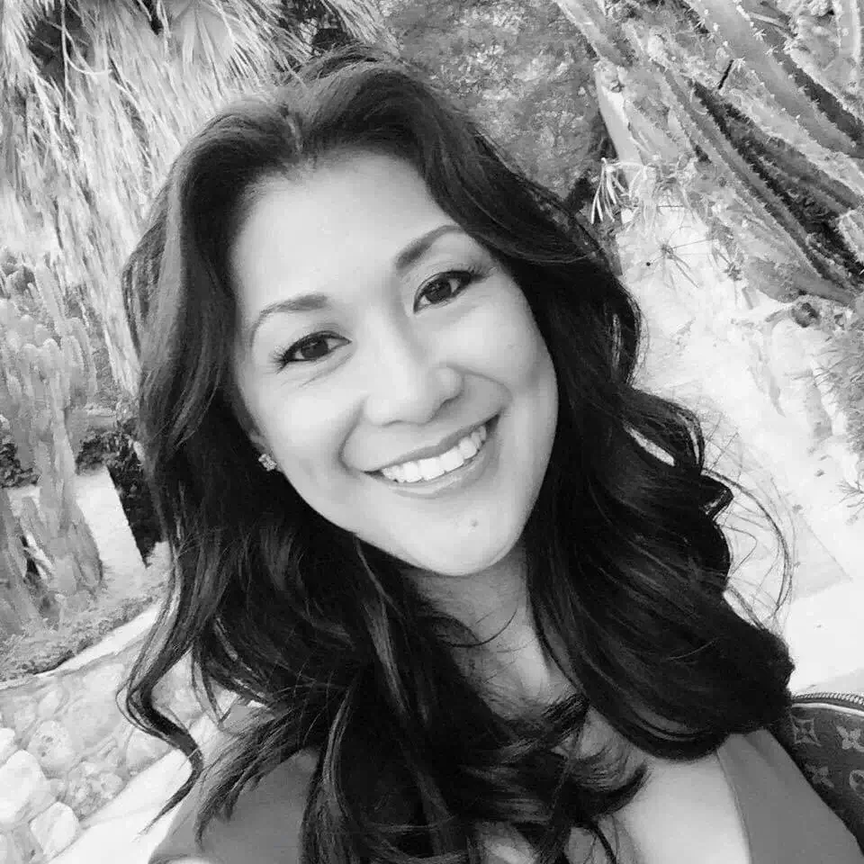 Black and white portrait of a woman with long, wavy dark hair smiling with a desert setting behind her.