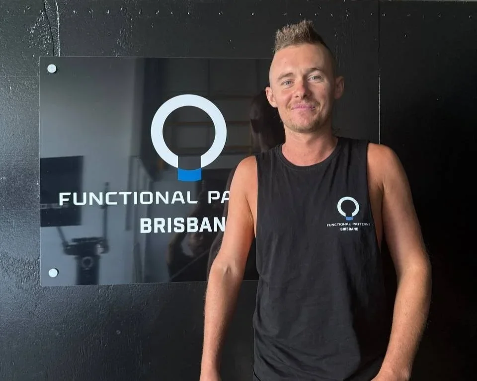 A man wearing a sleeveless black shirt with a logo standing in front of a sign that reads 'Functional Patterns Brisbane' with a circular logo.