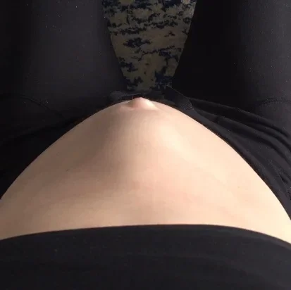 Close-up of a pregnant woman's belly, with the woman sitting down wearing black clothing.