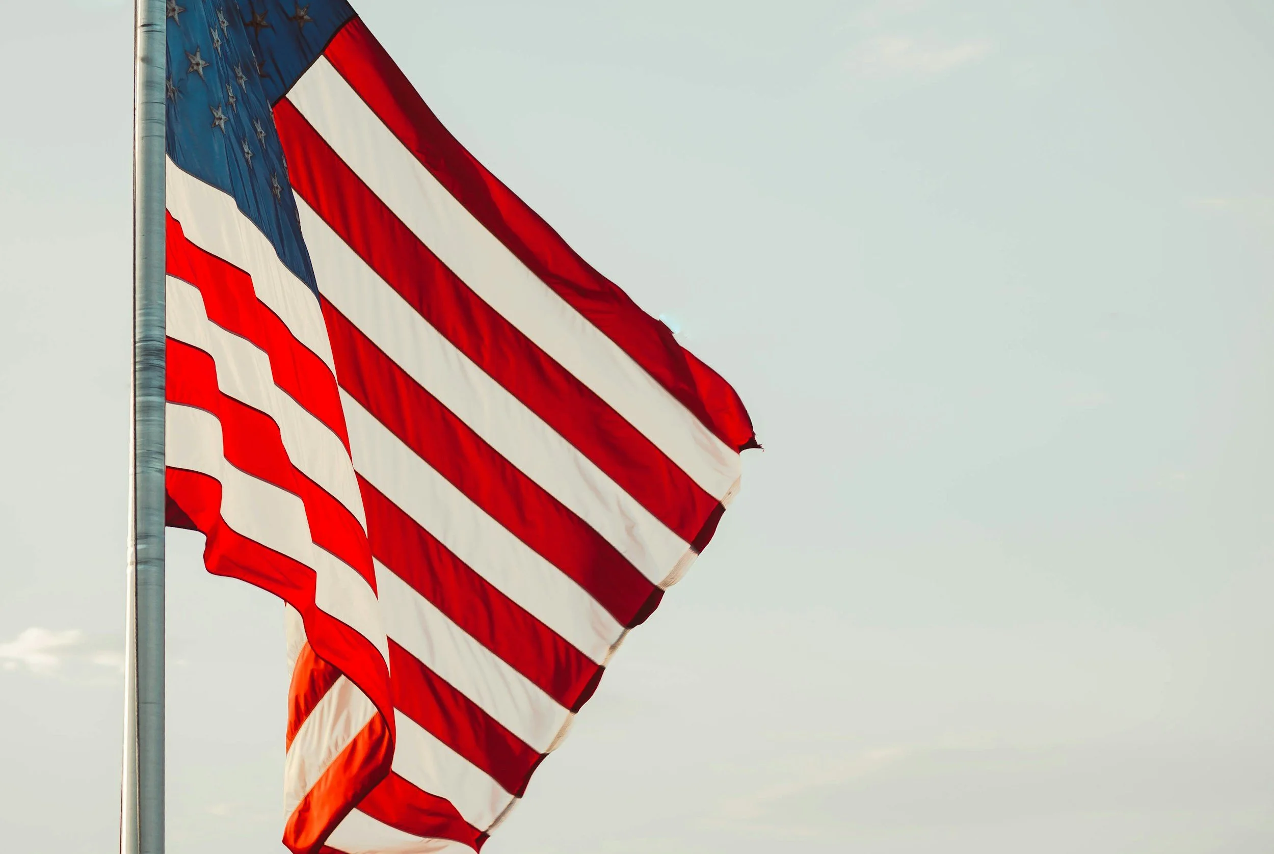 American flag flying on a flagpole against a cloudy sky.