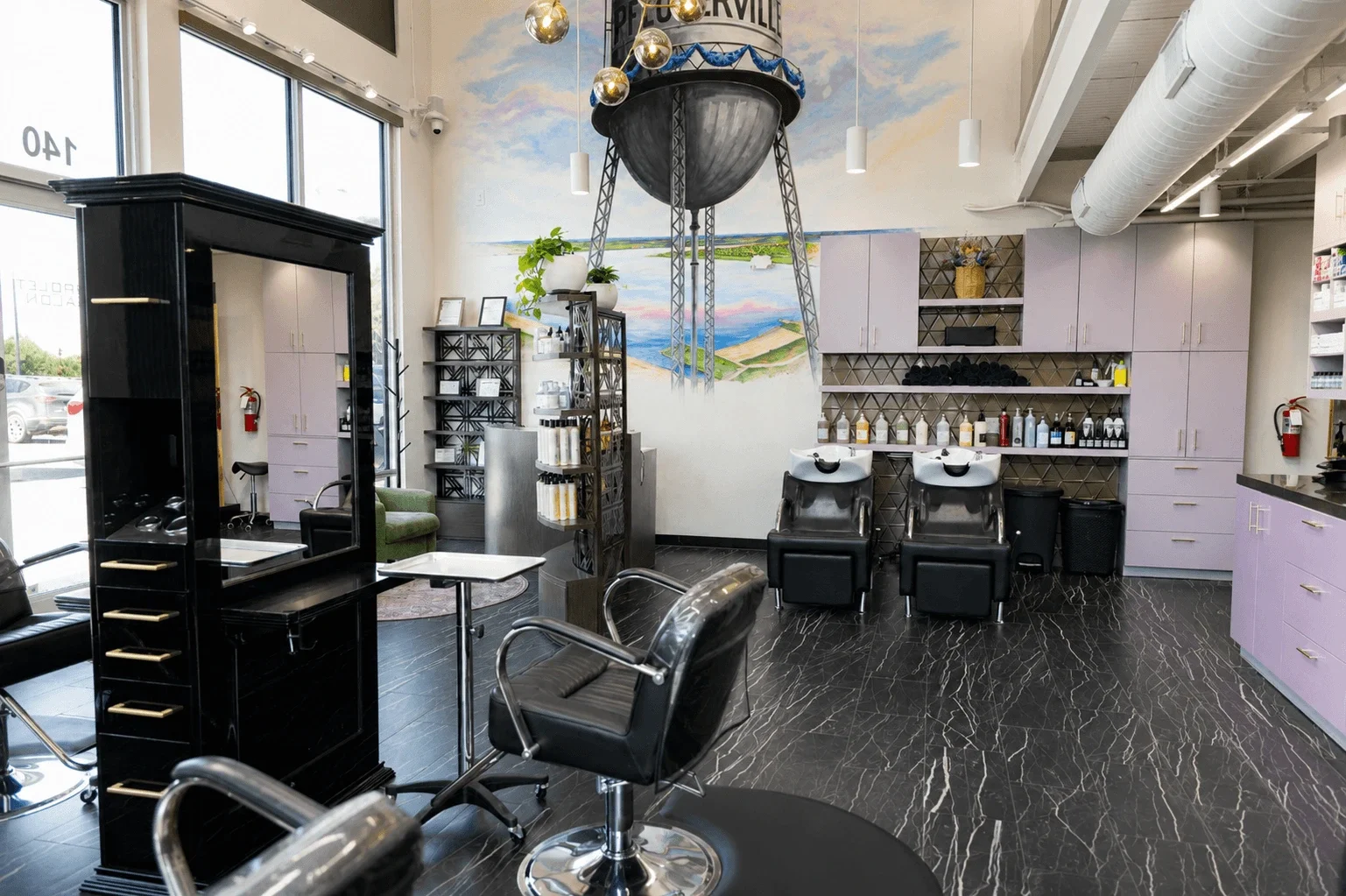 Interior view of a hair salon with styling chairs, hair washing stations, and shelves holding hair products, with a large mirror, a mural, and modern decor.