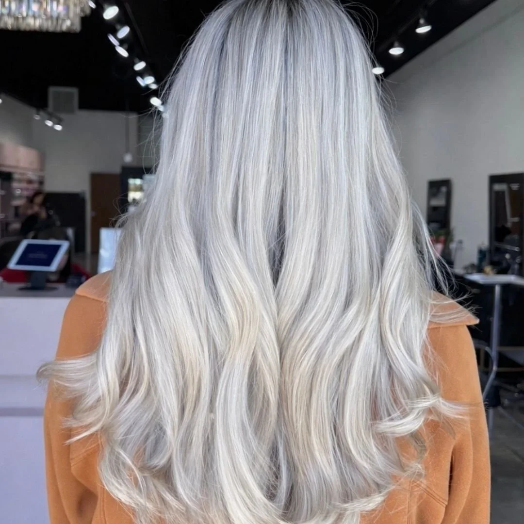 Back view of a woman with long, wavy, platinum blonde hair, wearing a tan or caramel-colored top at Spoleti Salon in Austin, Texas.