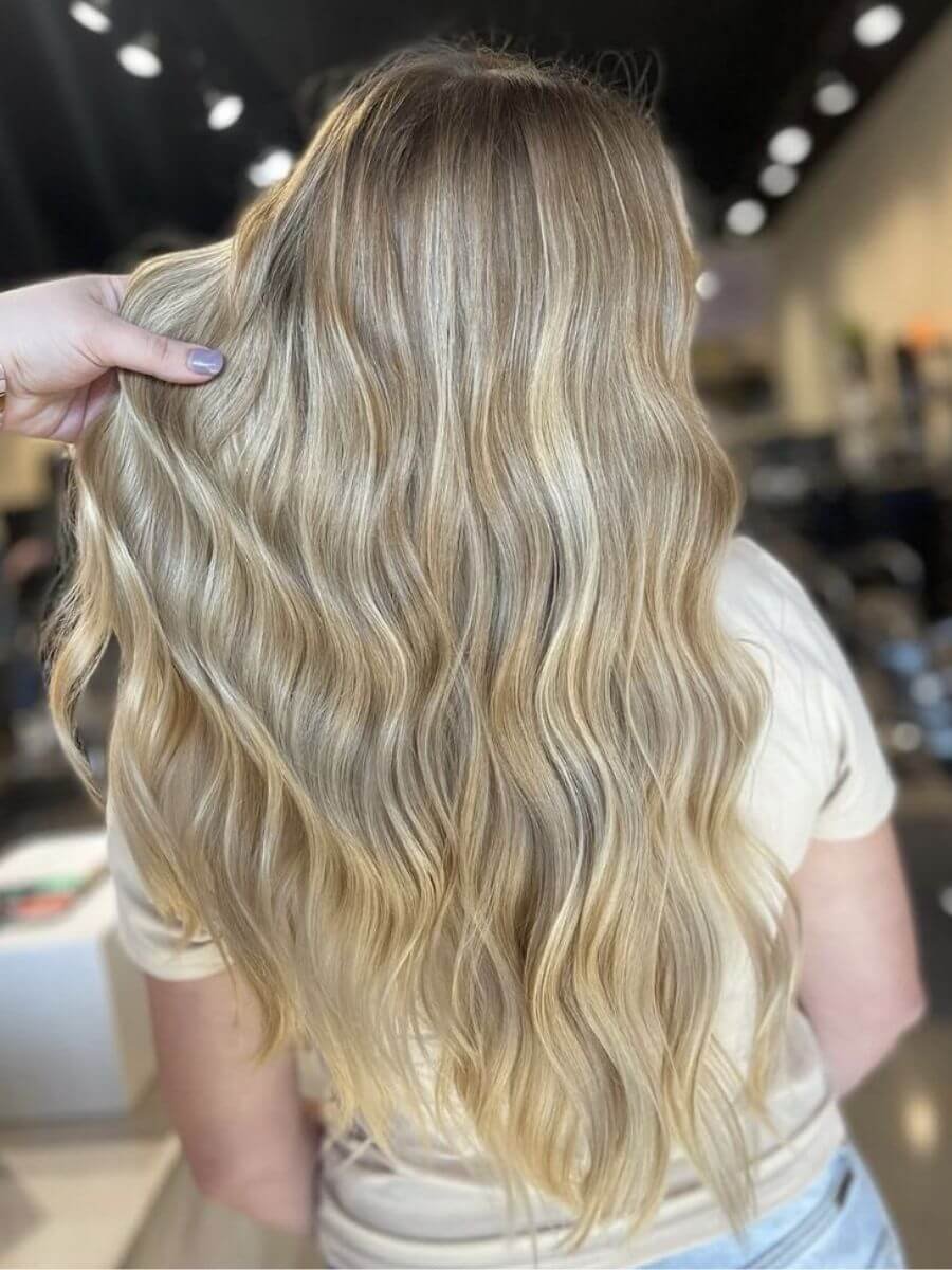Close-up of a person's long, wavy blonde hair held by someone, with a blurred background.
