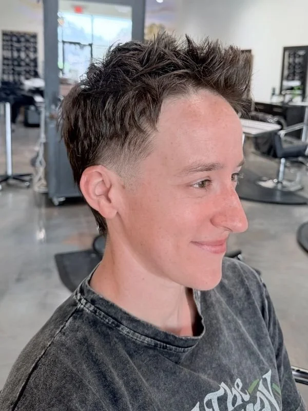Woman with short, layered haircut with shaved sides, smiling in a hair salon
