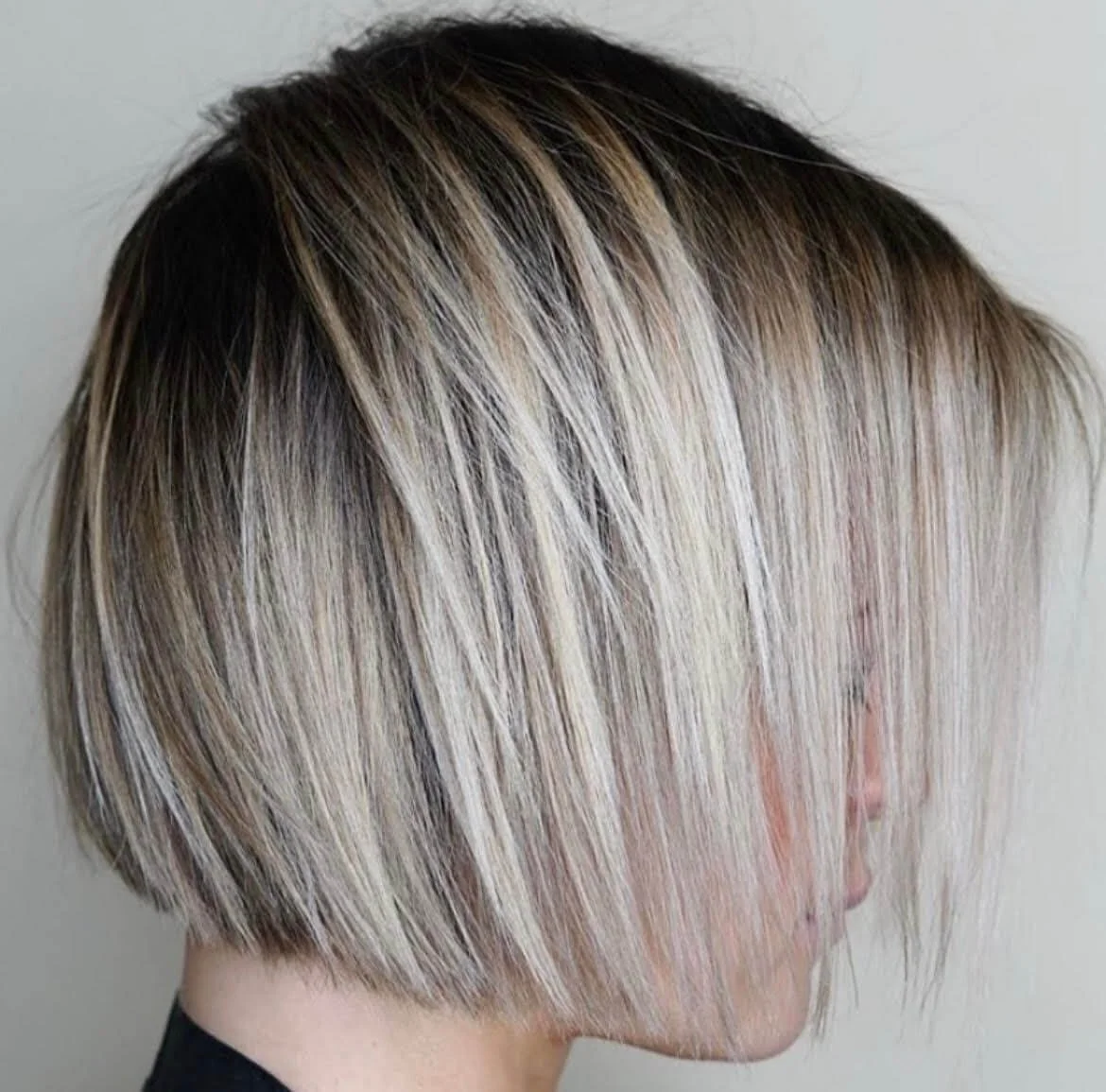 Side view of a woman with a short, layered bob haircut with blonde highlights and darker roots.