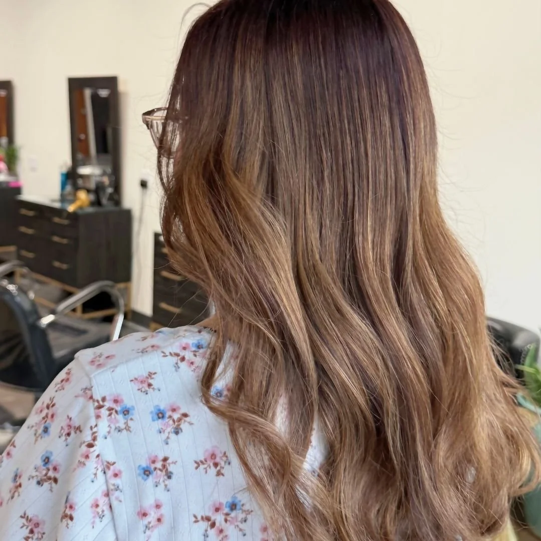 Back of woman with long, wavy, light brown hair, wearing glasses and floral-patterned top, at Spoleti Salon in South Austin, Texas.