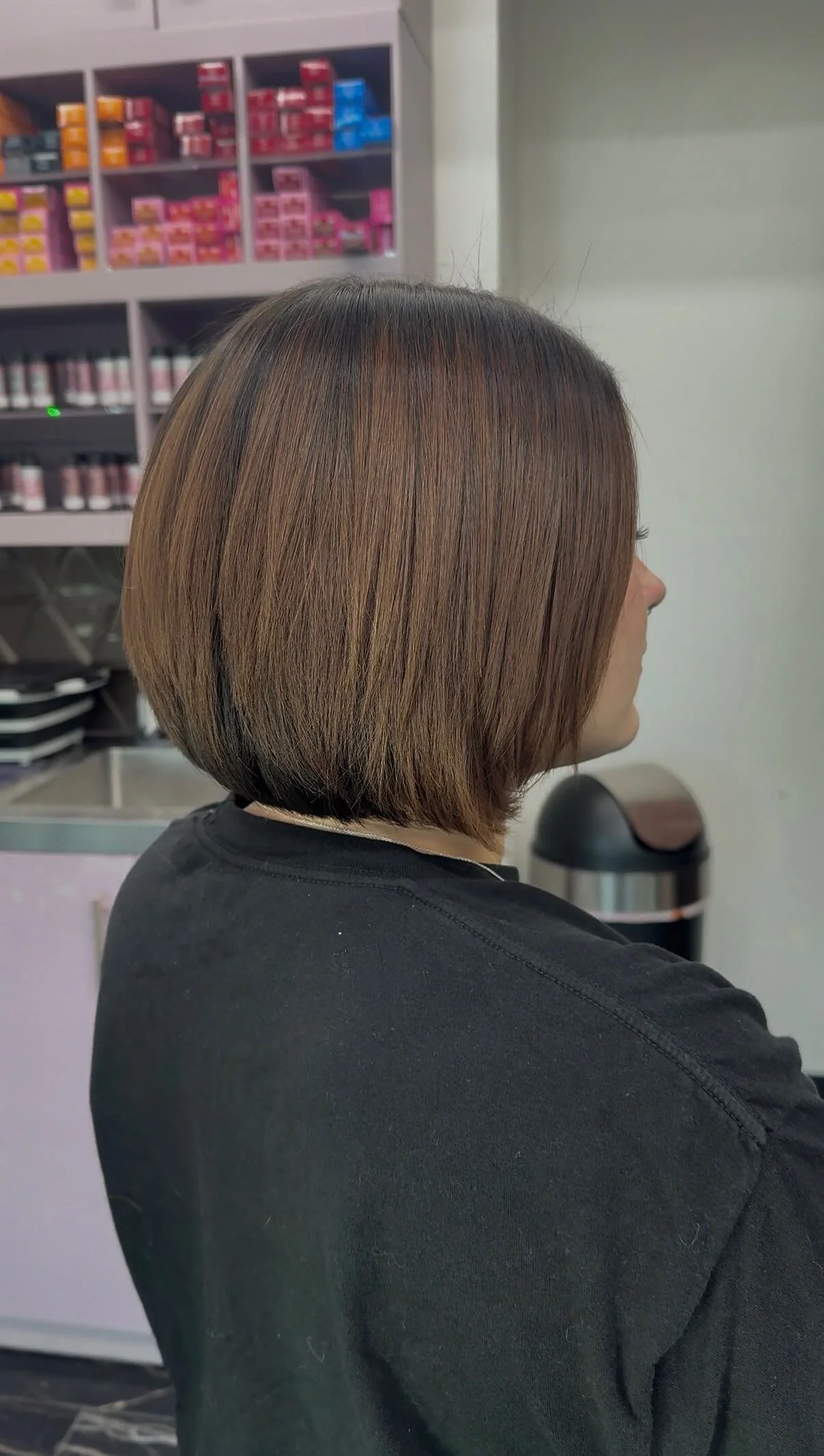 Side view of a woman with a neat, straight, shoulder-length bob haircut with light brown and dark brown highlights in a salon setting.