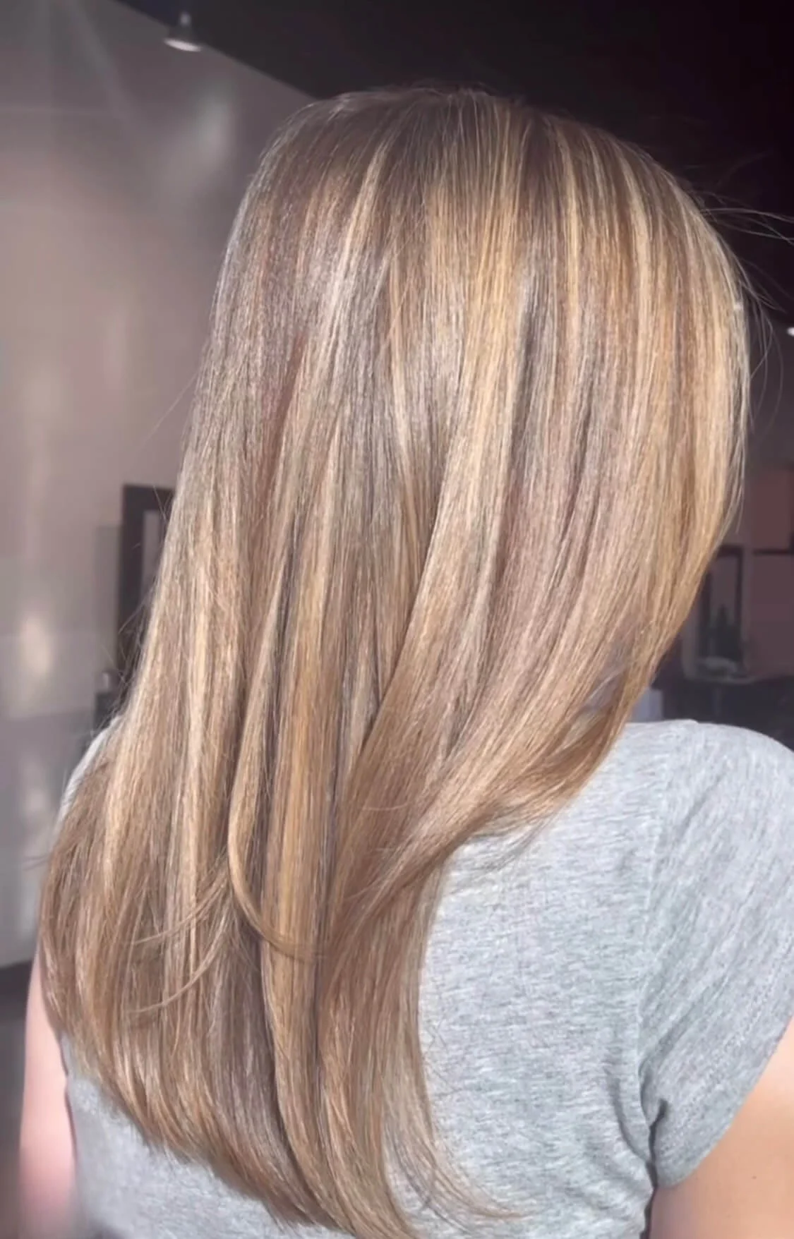 Back of a woman with long, straight blonde hair, wearing a light gray T-shirt.