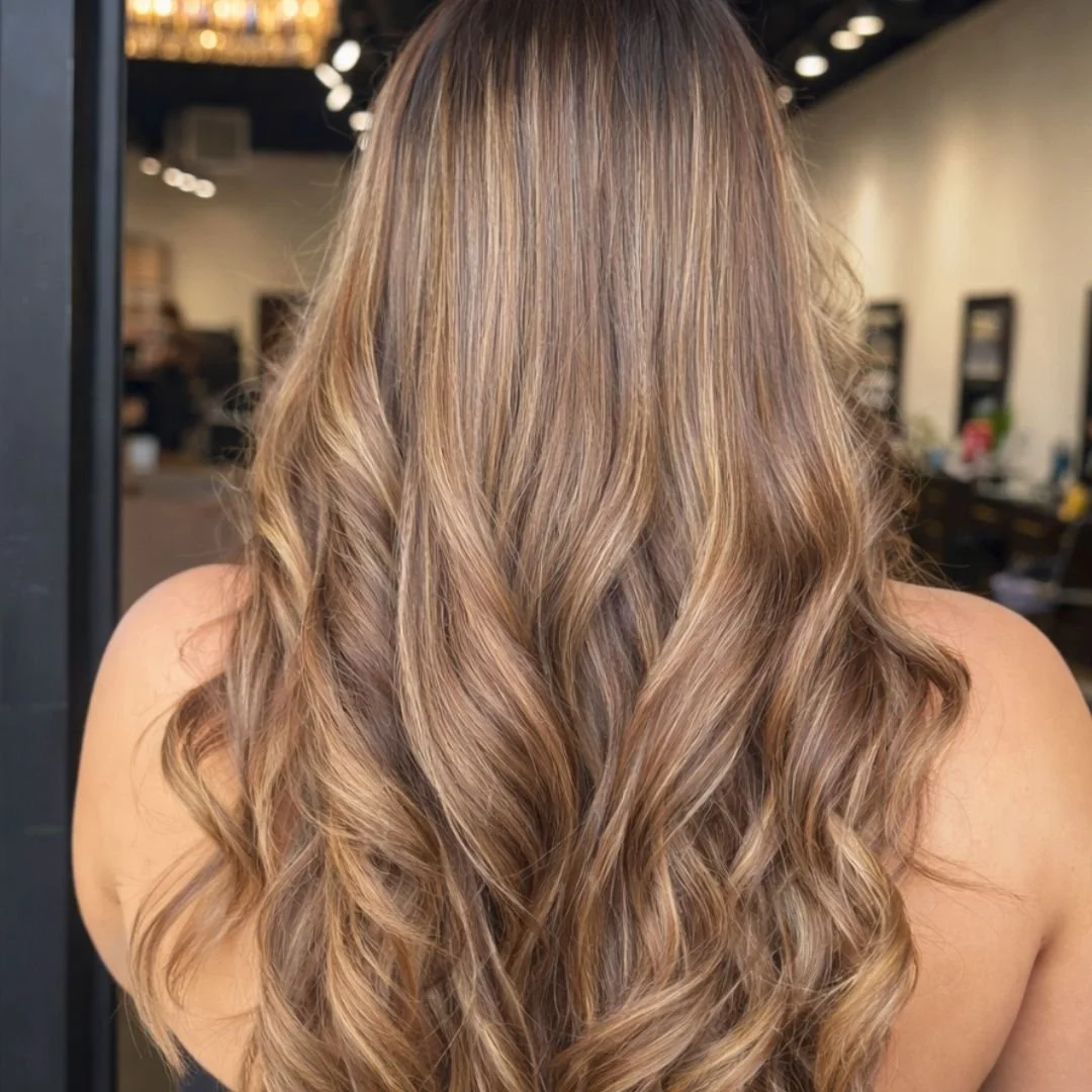 Back view of a woman with shoulder-length, wavy, light brown hair with blonde highlights, at a hair salon in Austin, Texas.