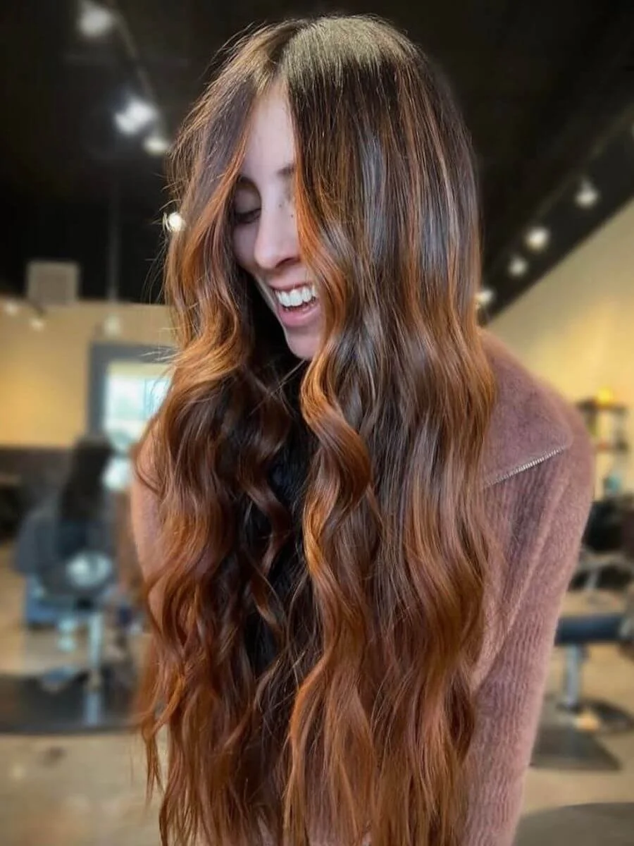 A woman with long, wavy, reddish-brown hair smiling in a salon or similar setting.