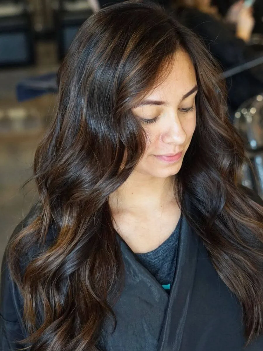 Young woman with long wavy brown hair in a salon or similar setting.