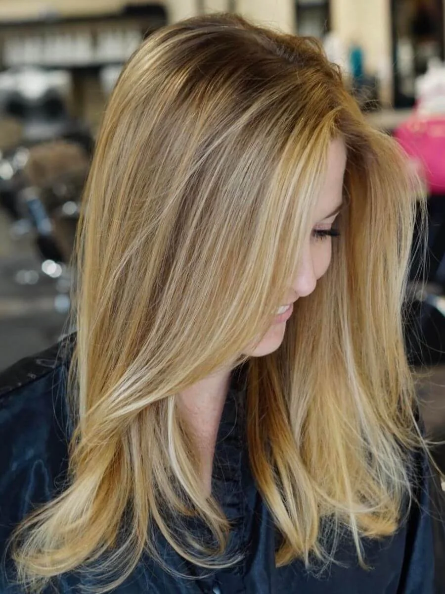 Side view of a woman with long, blonde, highlighted hair, partially covering her face, in a hair salon.