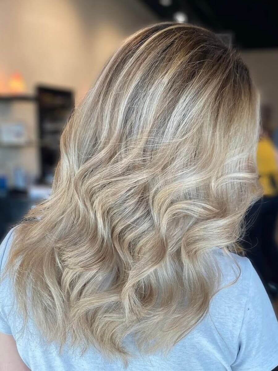 Blonde hair styled in loose waves with darker roots, viewed from the side.
