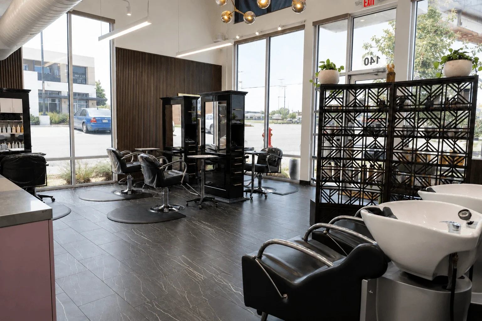 Interior of a modern hair salon with styling chairs, washing stations, large windows, and decorative plants.