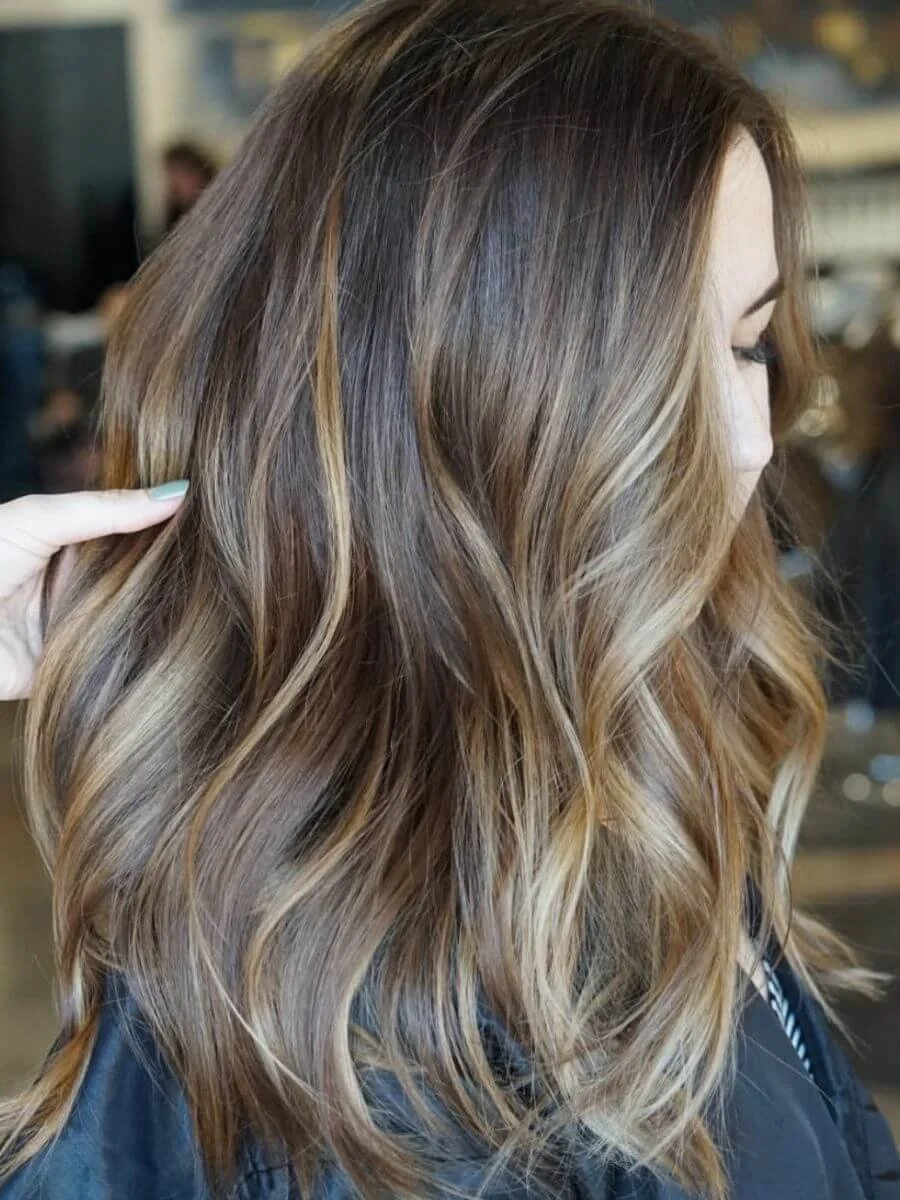 Close-up of a woman with shoulder-length, wavy, light brown to blonde ombre hair.