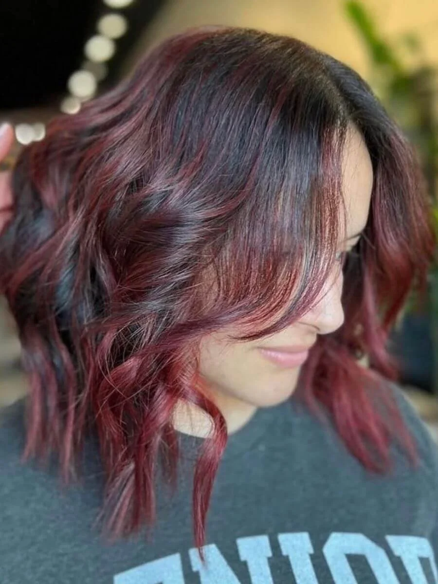 Side view of a woman with shoulder-length wavy hair dyed in shades of red and purple.