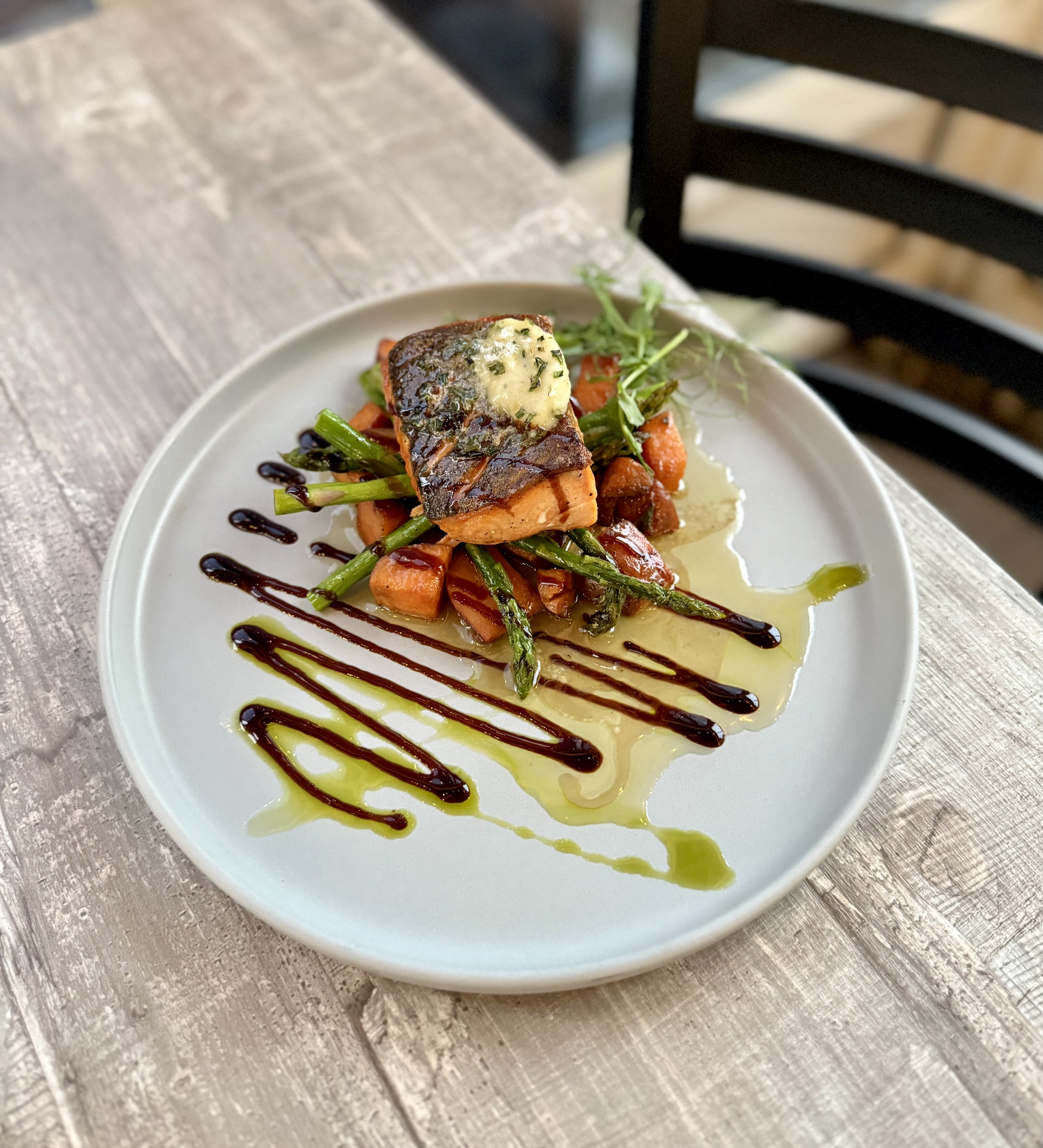 Pine Point Grill's pan-seared salmon entrée featuring roasted sage sweet potato, bourbon maple butter, grilled garlic asparagus, and balsamic glaze.