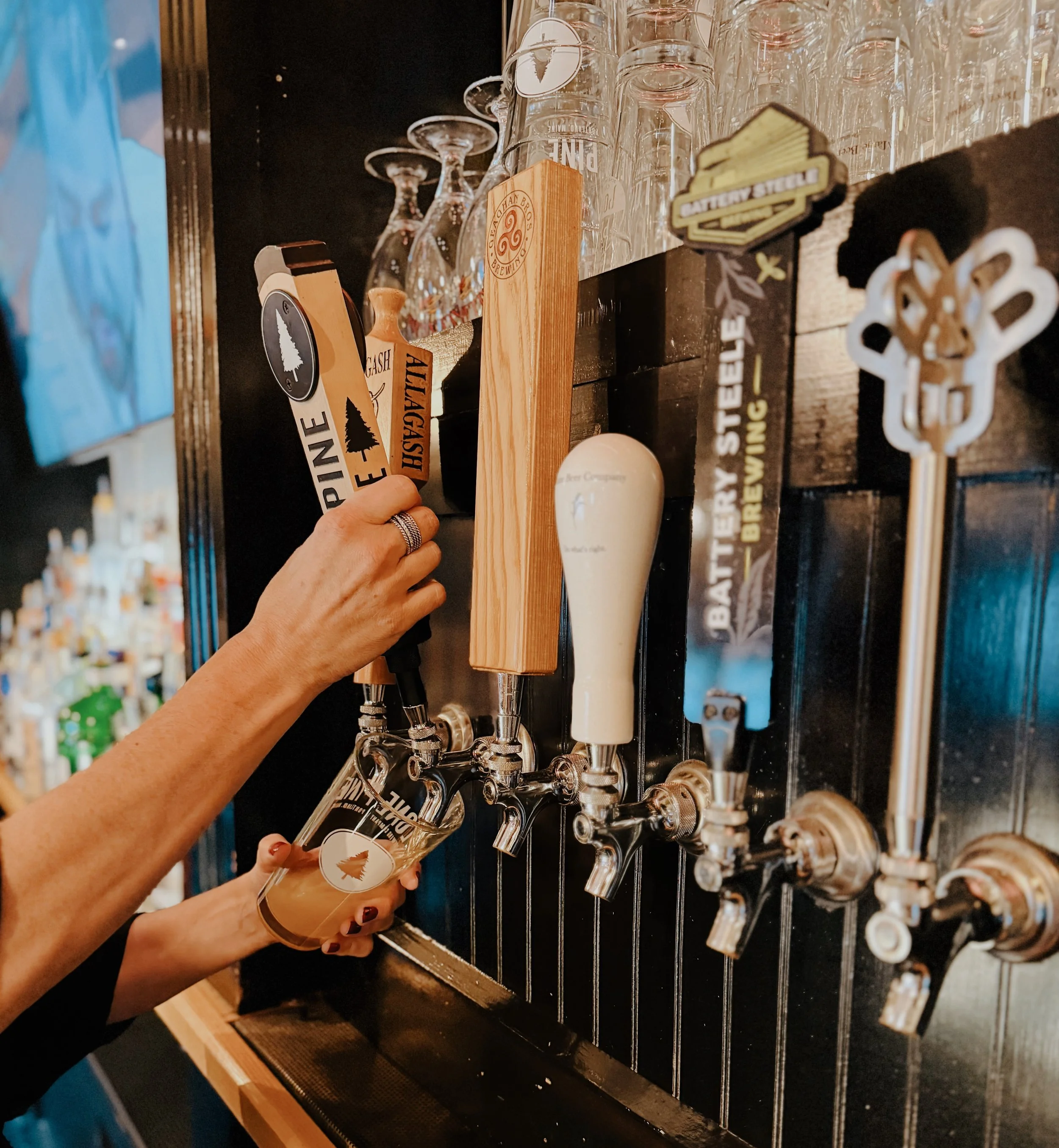 A bartender pouring beer from a tap into a glass at a bar with multiple beer taps.
