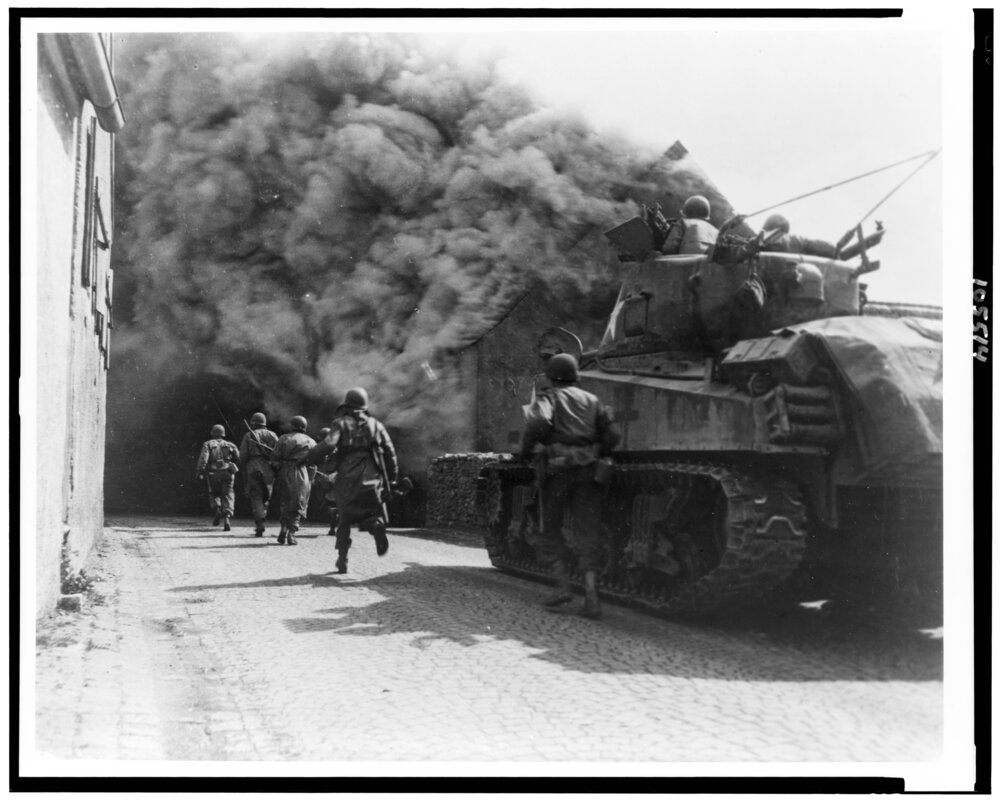 Soldiers of the 55th Armored Inf Bn, 22nd Tank Bn, 11th Armored Div US Third Army, run through smoke filled street in Wernberg Germany