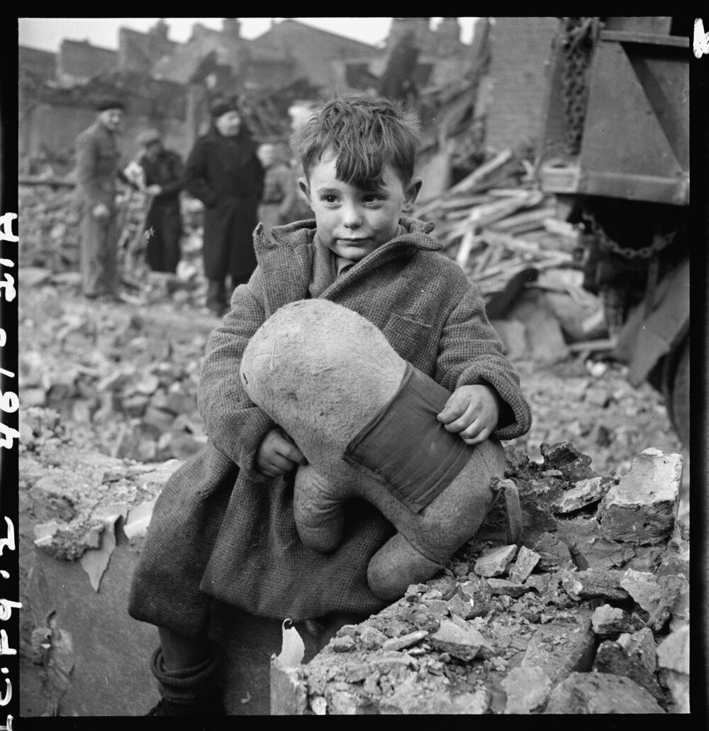 Abandoned boy holding a stuffed toy animal amid ruins following German aerial bombing of London