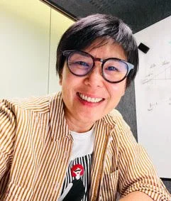 Person in striped shirt and wearing glasses in front of a whiteboard