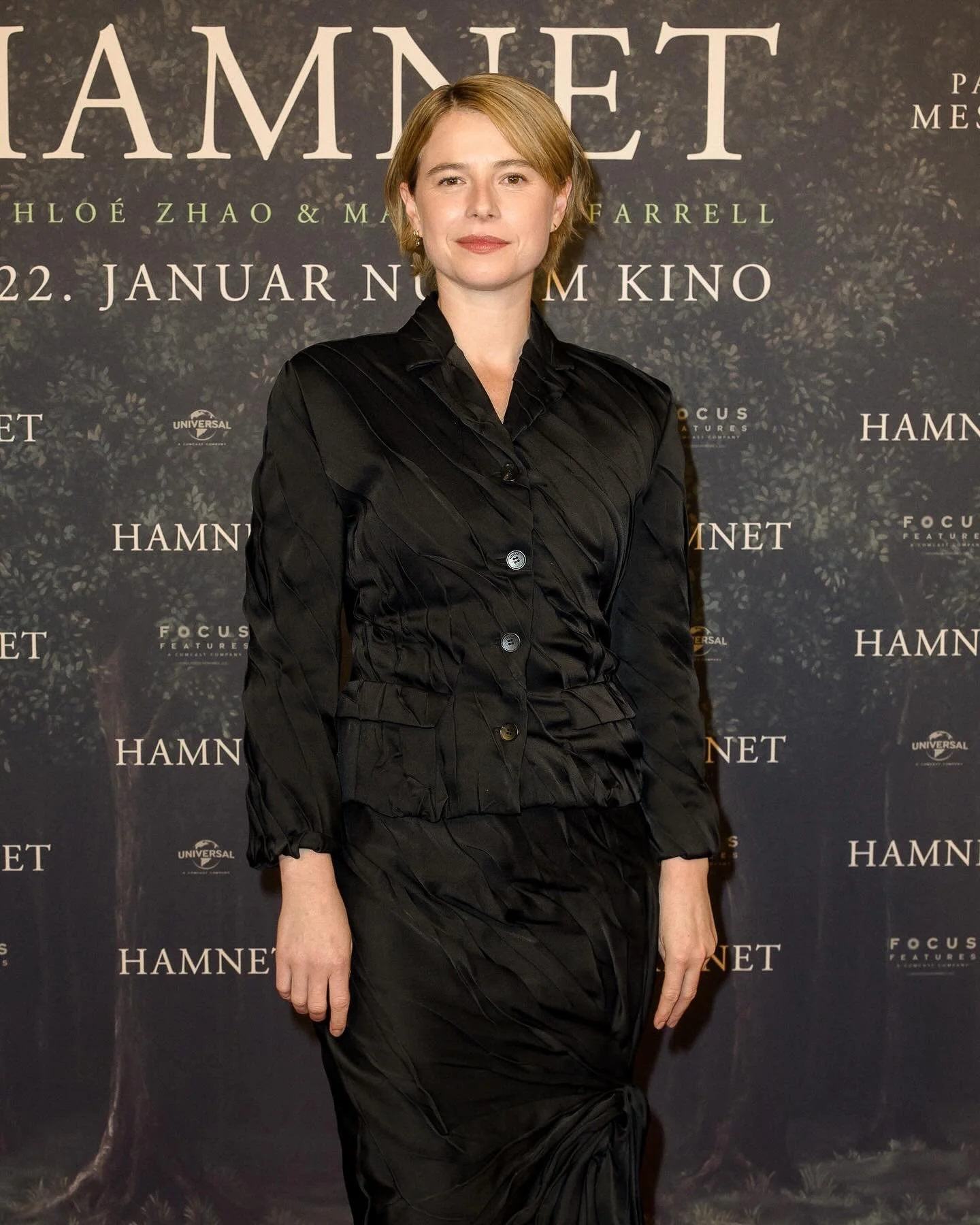 JESSIE BUCKLEY (@jessiebuckley) ปรากฏตัวในลุคเรียบโก้จาก Versace Spring Summer 2026 บนพรมแดงงาน Hamnet Premiere ณ กรุงเบอร์ลิน เมื่อวันที่ 8 ธันวาคม

นักแสดงสาวเลือกสวมเบลเซอร์ผ้าซาตินสีดำดีไซน์เดรป จับคู่กับกระโปรงมิดิอสมมาตรที่เข้าชุดกัน ถ่ายทอดเสน