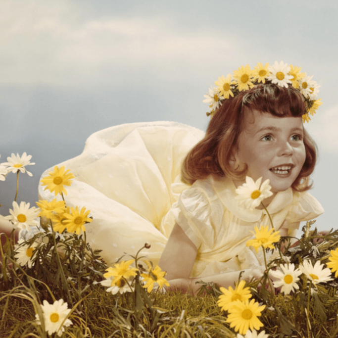 A young girl in a field of daisies with a crown.