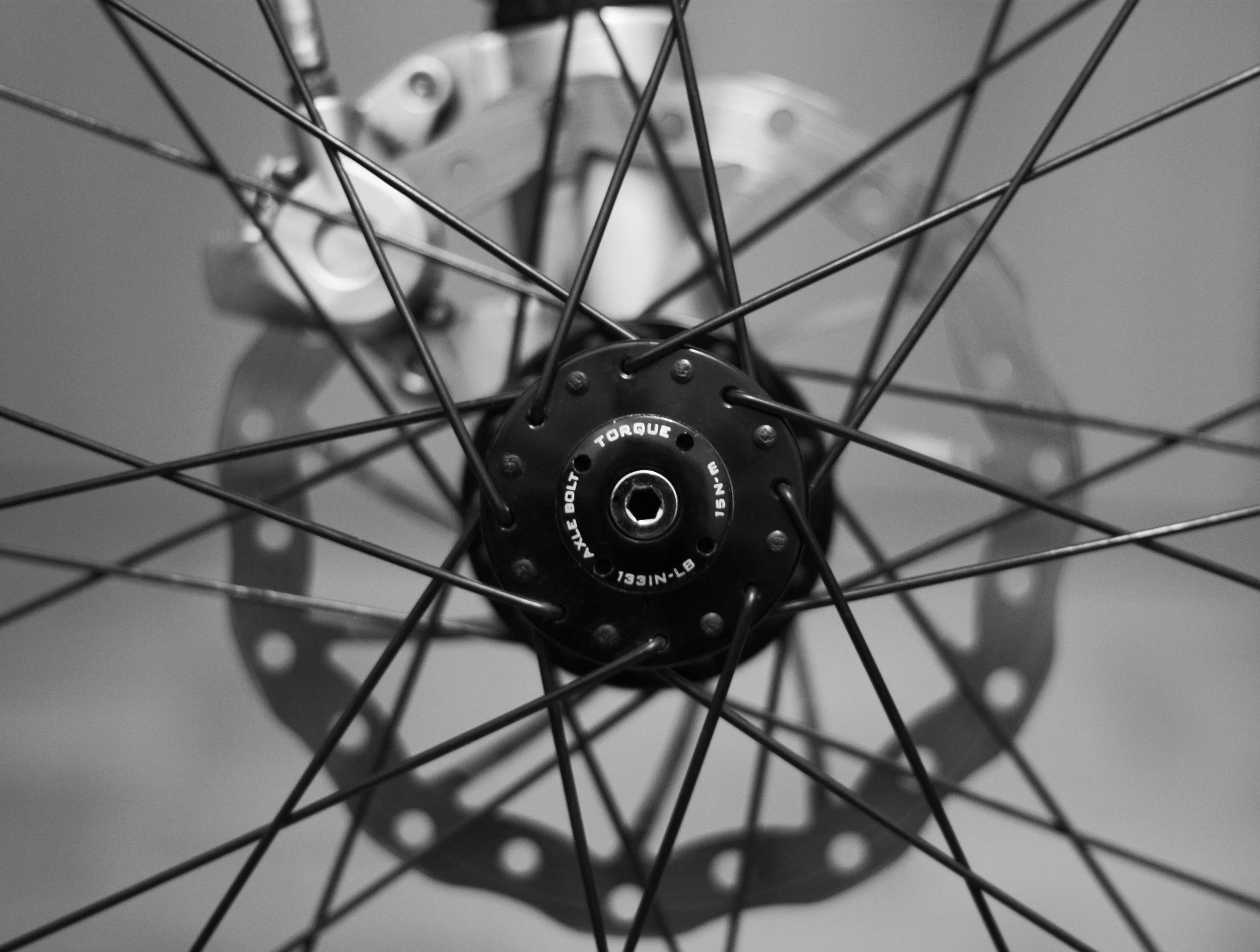 Close-up of a bicycle wheel with spokes, hub, and disc brake in black and white.