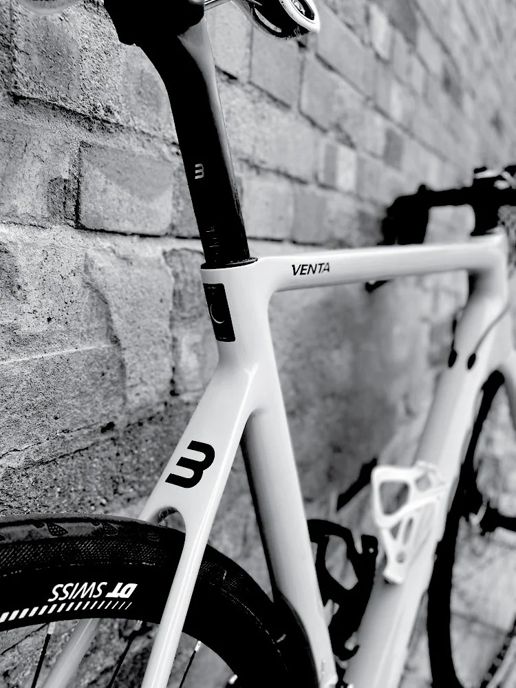 Close-up of a white and black road bicycle leaning against a brick wall, with a focus on the seat post, frame, and front wheel.