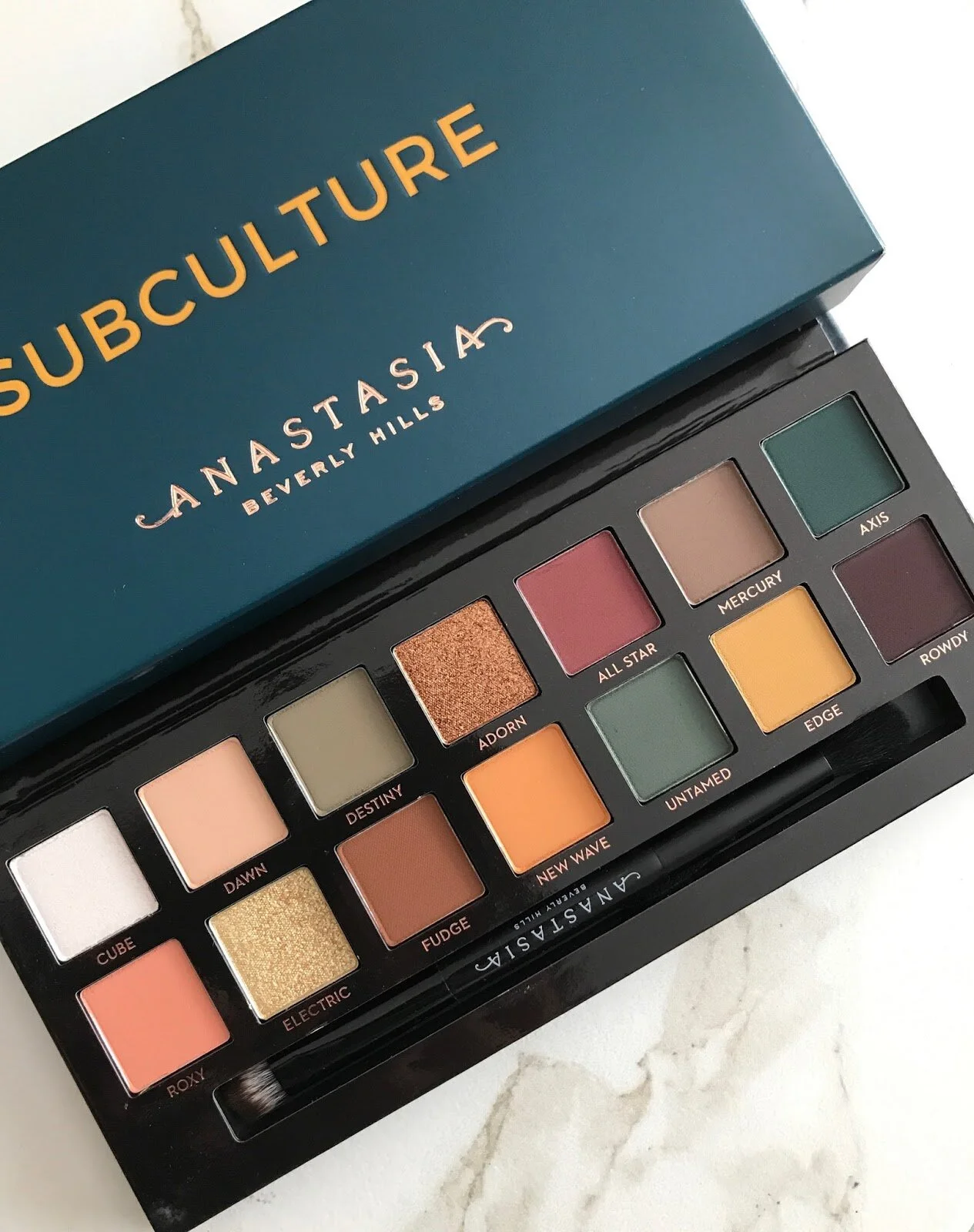 An Anastasia Beverly Hills Subculture eyeshadow palette showing various color shades including white, peach, gold, green, pink, and brown.