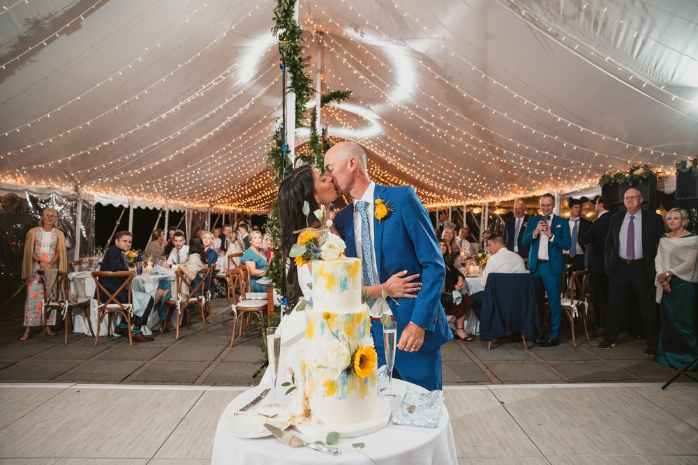 married-couple-kiss-during-cake-cutting-under-tent.jpg