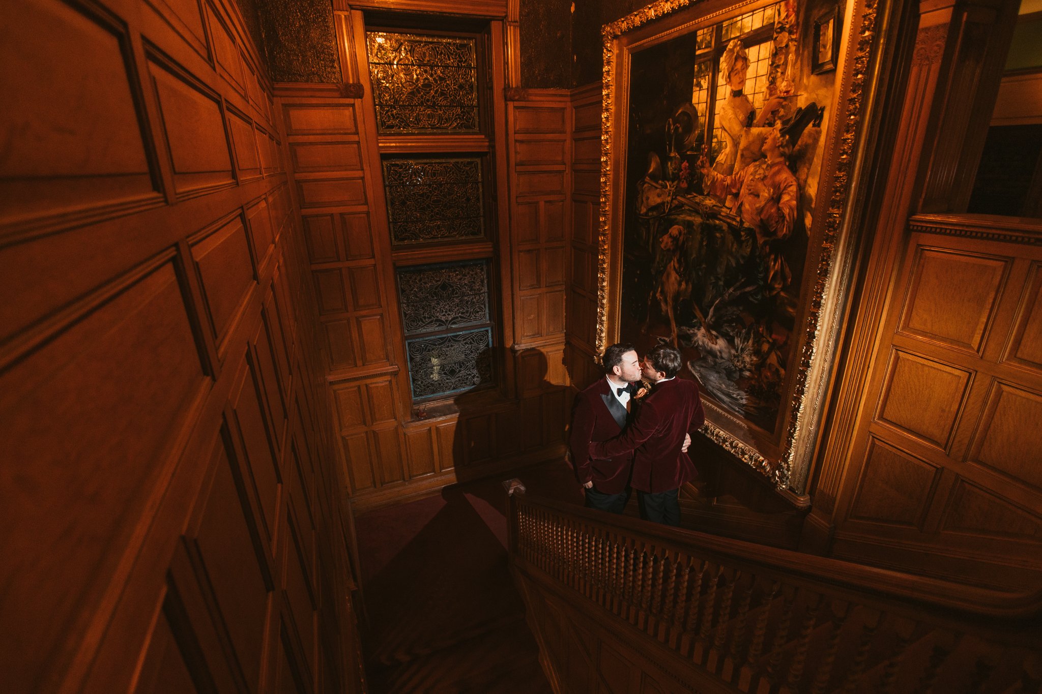 Two grooms share a dramatic nighttime portrait beside the restored 1890s oil painting at Stevens Estate at Osgood Hill in North Andover, Massachusetts.