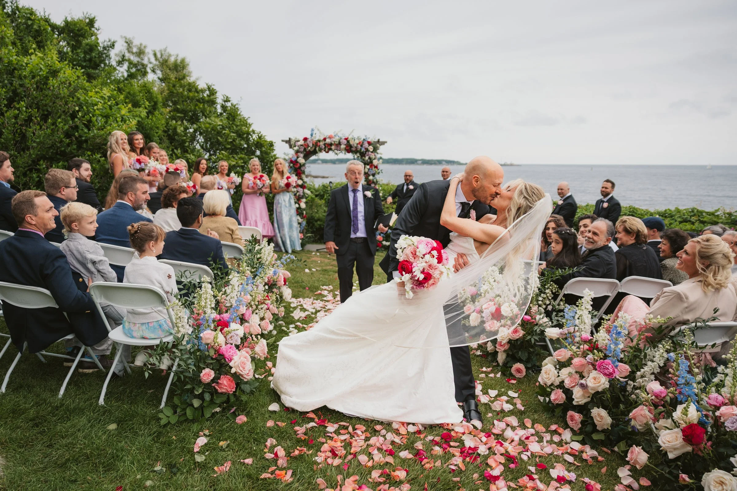 Bride and groom share a kiss dip at the end of the aisle during their oceanfront ceremony at Hammond Castle Museum in Gloucester, Massachusetts.