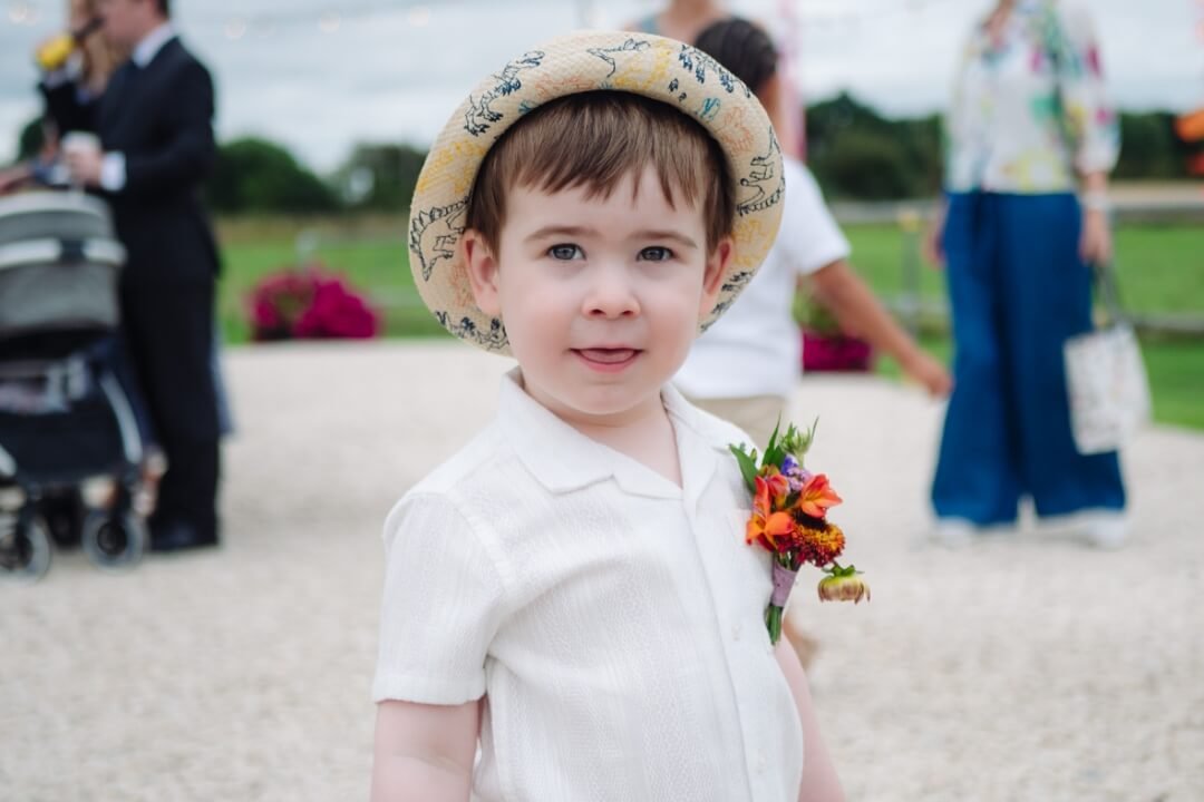 Young boy wearing a hat and floral boutonniere at outdoor wedding