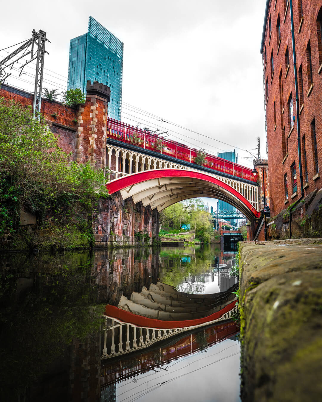 Red Castlefield bridge in Manchester reflected in the canal with the Hilton Hotel in the distance