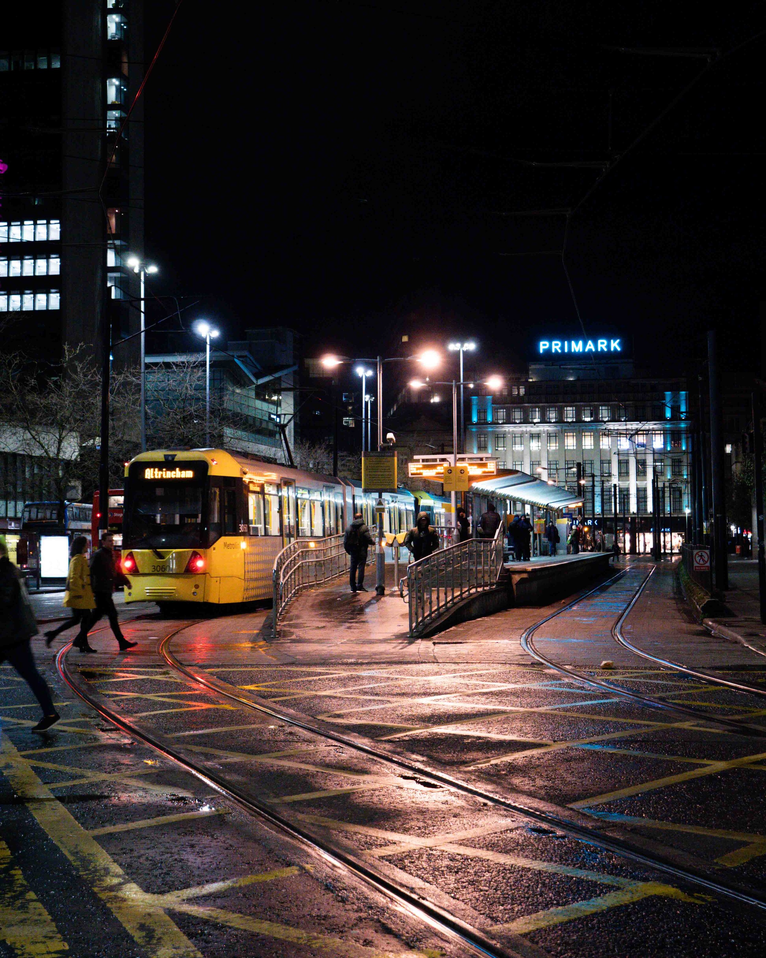 Manchester Piccadilly tram stop at night with a yellow tram picking up passengers, free stock photography.jpg