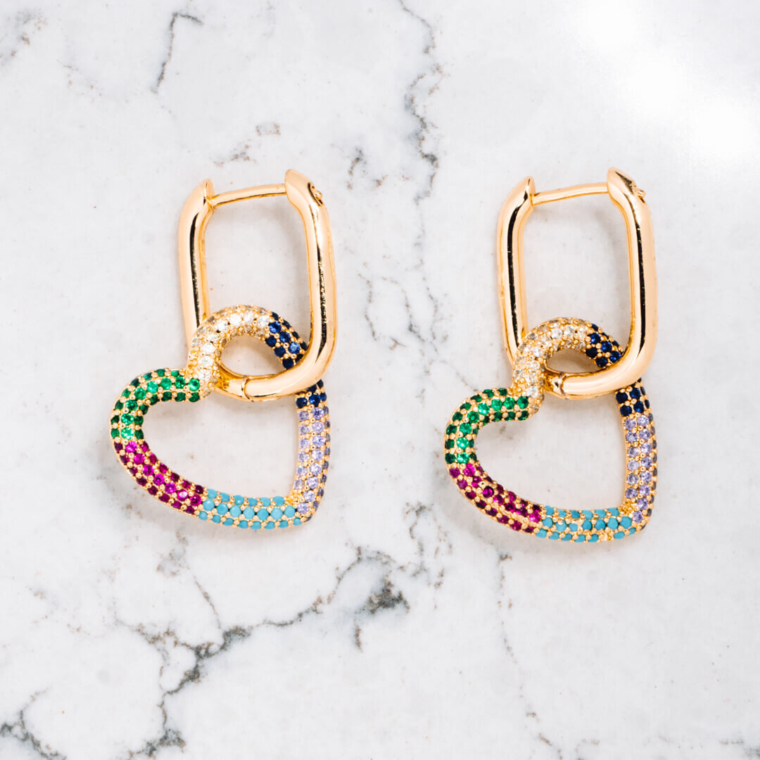 Product photography of two heart shaped earrings with multicoloured diamonds on a white marble background