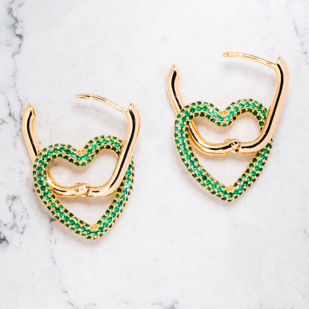 Product photography of two heart shaped earrings with green diamonds, on a white marble background