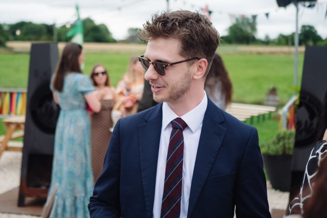 Wedding guest in navy suit and sunglasses at outdoor ceremony